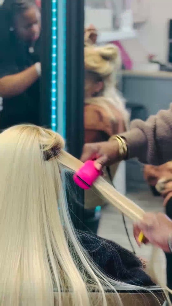 A stylist blow-drying a client at the mirror
