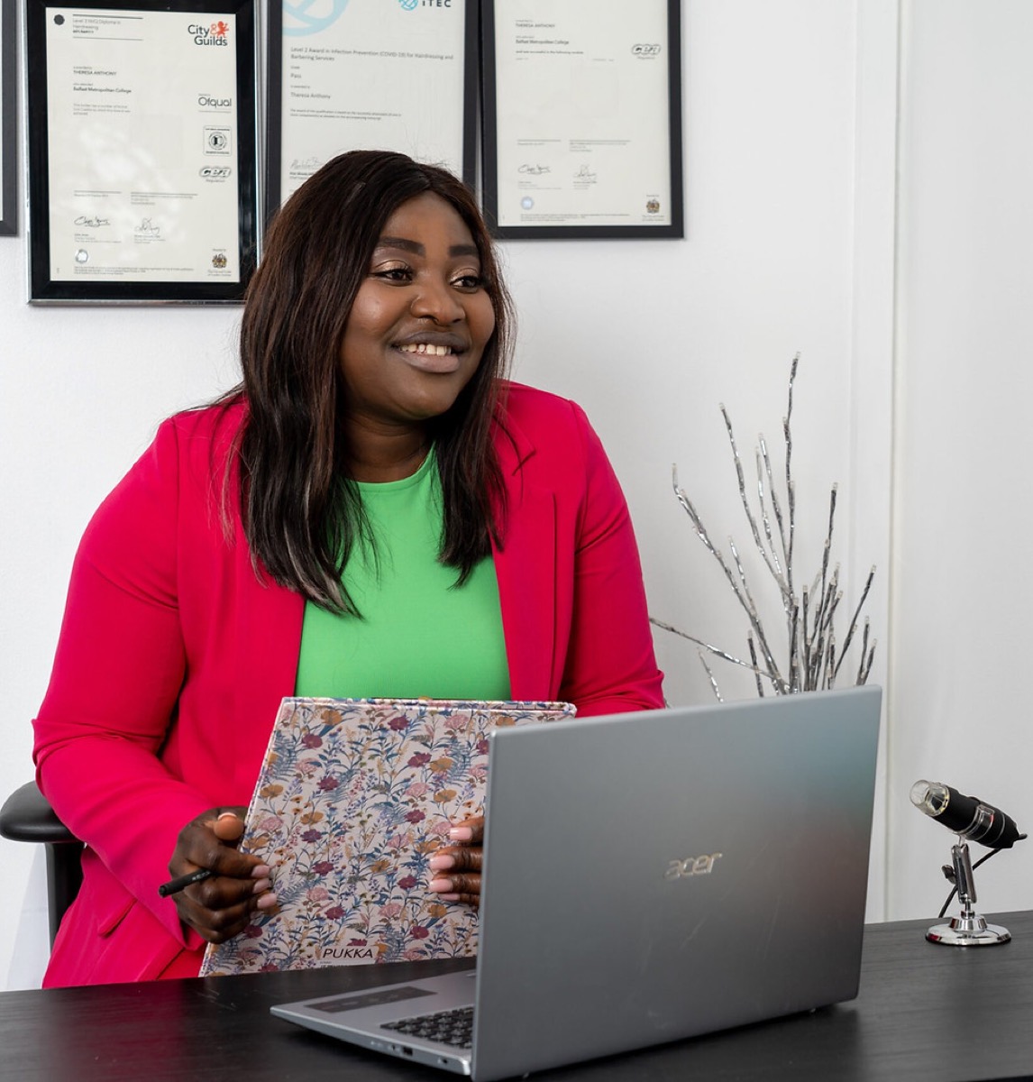 Theresa Anthony, certified trichologist and founder of Tess Hair & Scalp Clinic, at her consultation desk beside a digital trichoscope, with her framed trichology certifications on the wall behind her